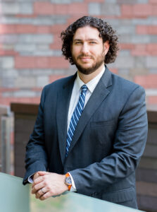 Picture of Justin Kelsey, Caucasian male with curly hair and beard in a grey suit