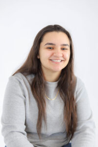 Picture of Mel Neves, long brown hair with grey shirt and gold chain